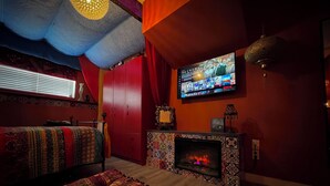 Une pièce chaleureuse avec une cheminée, un téléviseur fixé au mur et un lit agrémenté d’une literie à motifs.