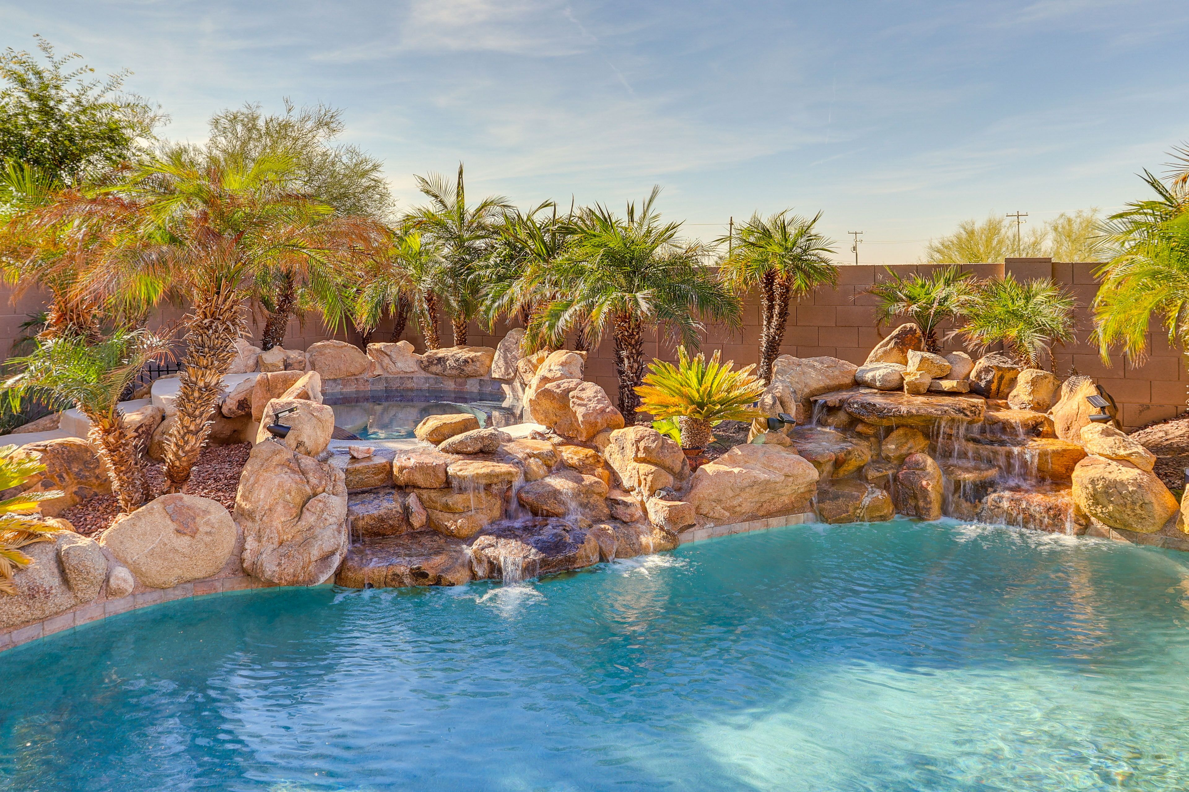 A pool with clear blue water, surrounded by large rocks and palm trees.