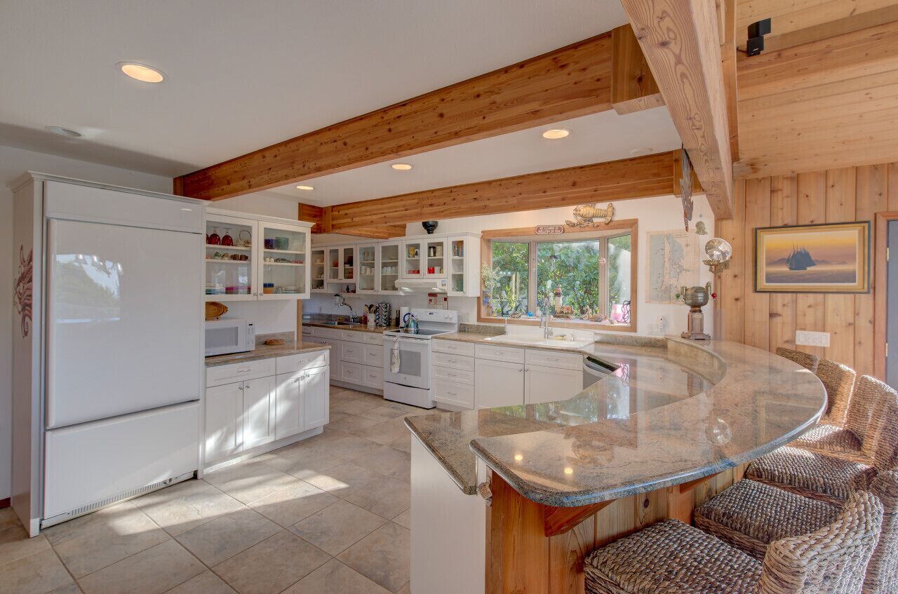Une cuisine moderne avec des meubles blancs, un îlot en granit et un plafond en bois.