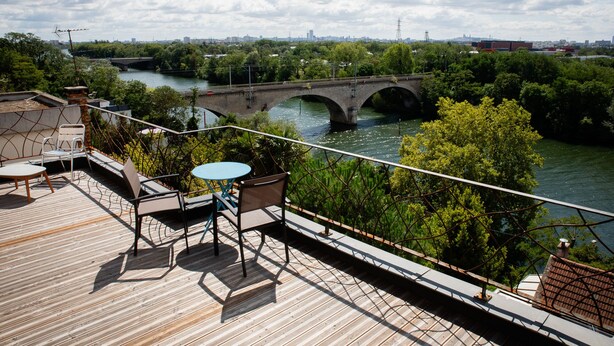 A wooden deck with outdoor furniture overlooking a river and a bridge. - L'Atelier sur Seine (Epinay-sur-Seine)