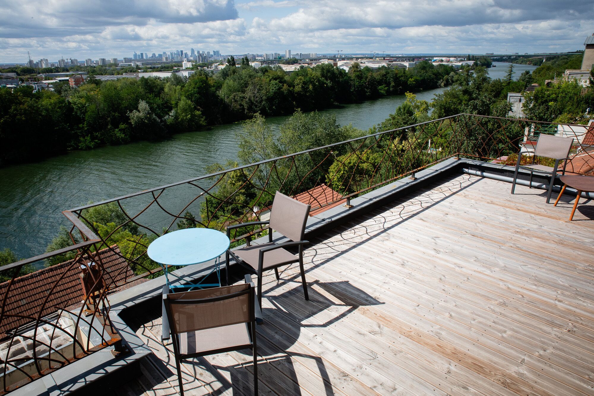 A deck with outdoor seating, overlooking a river and city skyline.