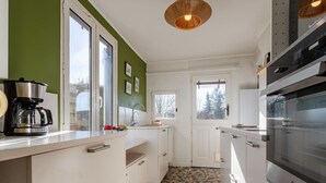 Eine moderne Küche mit weißen Schränken, einer Kaffeemaschine, Fliesenboden und einem Fenster mit Blick auf Bäume.