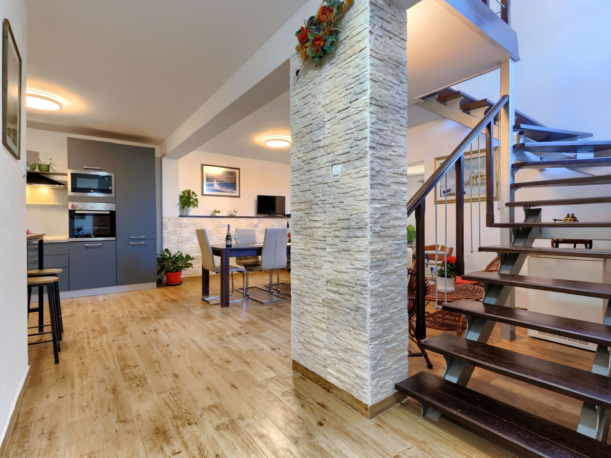 A modern kitchen with built-in appliances, a dining area with a table and chairs, and a staircase leading to an upper level.