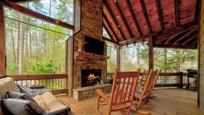 A wooden deck with a stone fireplace, a sofa with cushions, and a wooden rocking chair.