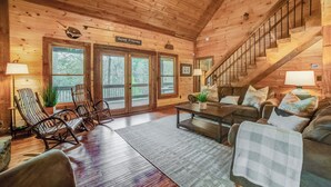 A cozy cabin interior with wooden walls, a staircase, a rocking chair, a sofa, and a coffee table.