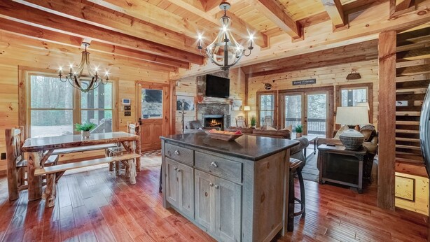 A wooden cabin interior with a large dining table, kitchen area, and a fireplace.