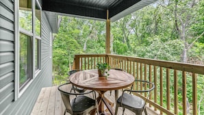 Une terrasse en bois avec une table ronde et des chaises, entourée d’une rambarde, donnant sur une zone boisée.