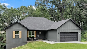 Une maison moderne à deux étages, avec une façade de couleur gris foncé, un garage et un porche à l’avant, agrémenté d’un banc.