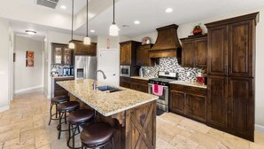 A kitchen with a central island, bar stools, dark wooden cabinets, stainless steel appliances, and pendant lighting. - A Dunes Oasis | Private Pool | Near Sand Hollow (Hurricane)