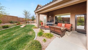 A residential patio with a barbecue grill, outdoor seating, and a well-maintained lawn. - A Dunes Oasis | Private Pool | Near Sand Hollow (Hurricane)