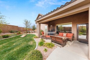 A residential patio with a barbecue grill, outdoor seating, and a well-maintained lawn.