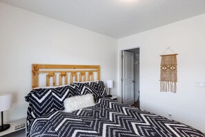 A bedroom with a bed, a headboard, a wall-mounted macrame decoration, and a door. - Red Riviera | Prime Location For Adventure! (Washington)