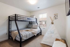 Een stapelbed met gestreepte beddengoed, een witte tipi en een raam met jaloezieën.