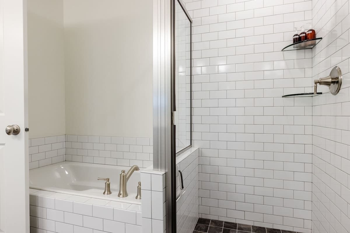 Un baño con bañera, cabina de ducha de cristal y pared de azulejos blancos.