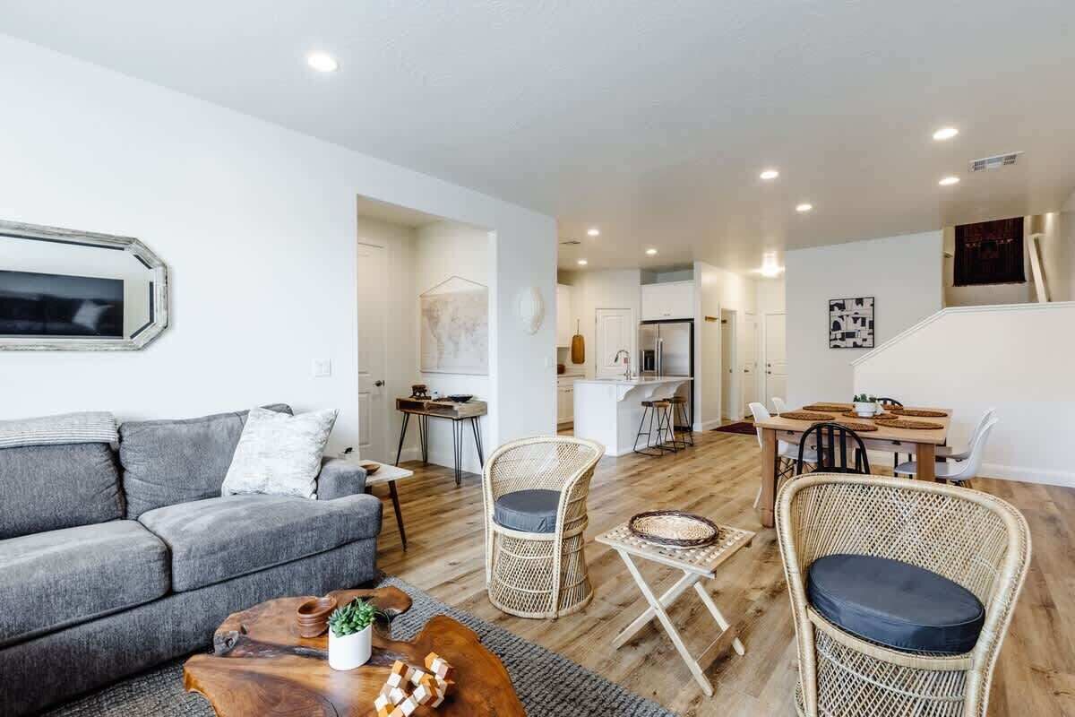 Un salon moderne avec un canapé, une table basse et des fauteuils en osier. On aperçoit à l’arrière-plan un coin repas avec une table et des chaises.