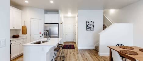 A modern kitchen with white cabinetry, a central island with stools, and a wooden dining table with chairs.