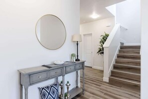 A hallway with a grey console table, a round mirror, a floor lamp, and a staircase with wooden steps. - Desert Riviera | Prime Location For Adventure! (Washington)