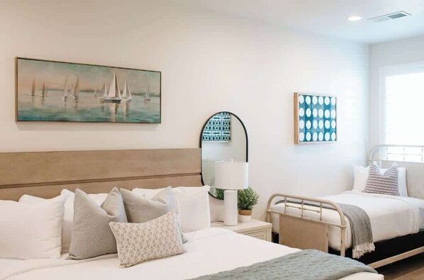 A hotel room with a bed, a bedside table, a lamp, a mirror, and a painting of sailboats.