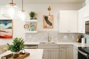 A kitchen with white cabinets, a stainless steel sink, and a hanging light fixture.