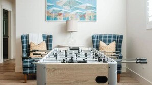 Ein Zimmer mit einem Kicker, zwei karierten Sesseln, einem Gemälde und einer Lampe.