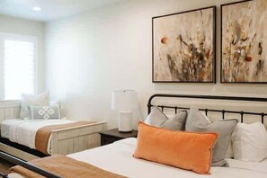 A hotel room with two beds, a bedside table, a lamp, and abstract artwork on the wall.
