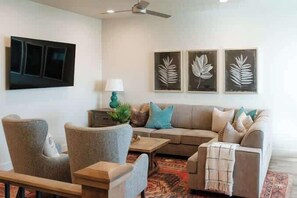 A living room with a sofa, armchairs, a coffee table, and a TV mounted on the wall.