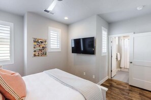 A bedroom with a bed, a mounted TV, and a door leading to a bathroom.