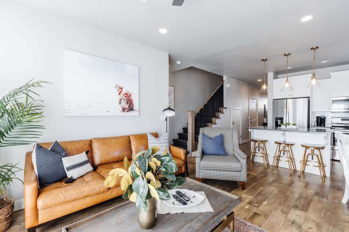 A modern living room with a leather sofa, a coffee table, and a staircase leading to a kitchen area.