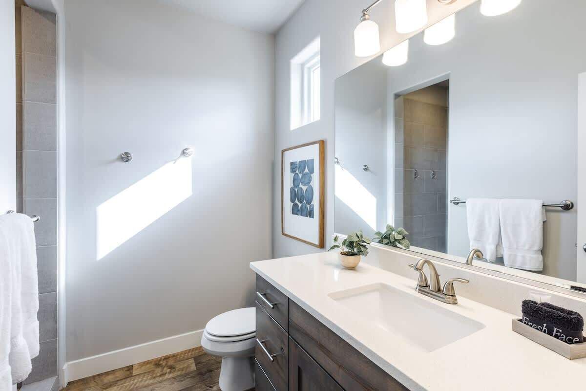 Une salle de bain moderne avec un lavabo blanc, des meubles en bois foncé, un grand miroir et un tableau encadré au mur.