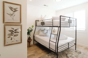 A bunk bed with a metal frame, white bedding, and a small side table with a plant.