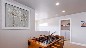 A room with a foosball table, a painting on the wall, and a laundry area.
