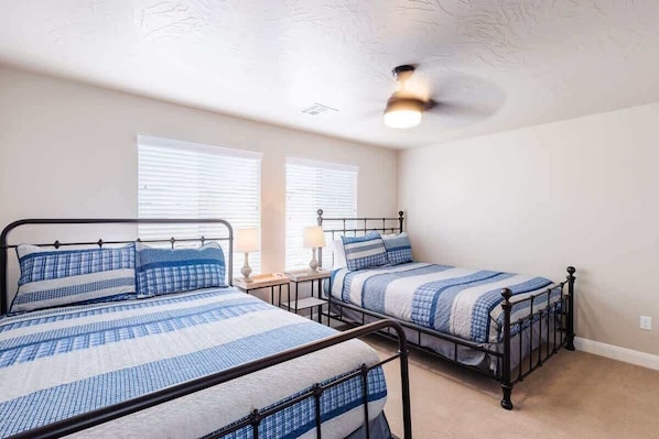 Een slaapkamer met twee bedden, elk op een metalen frame en met blauw beddengoed. Er zijn twee nachtkastjes met lampen, en de kamer heeft een plafondventilator.