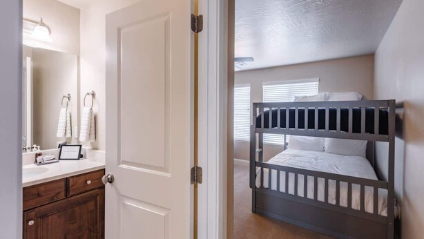 A bedroom with a bunk bed, a white door, a bathroom with a mirror, and a sink.