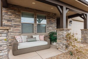 A covered porch with a wicker sofa, stone walls, and a potted plant.