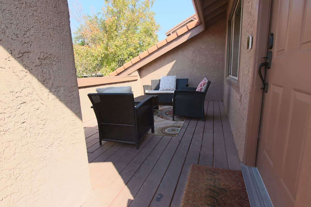 A covered outdoor patio with a table and chairs, a door, and a view of trees.