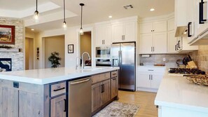 Una cocina moderna con una isla central, electrodomésticos de acero inoxidable e iluminación colgante.