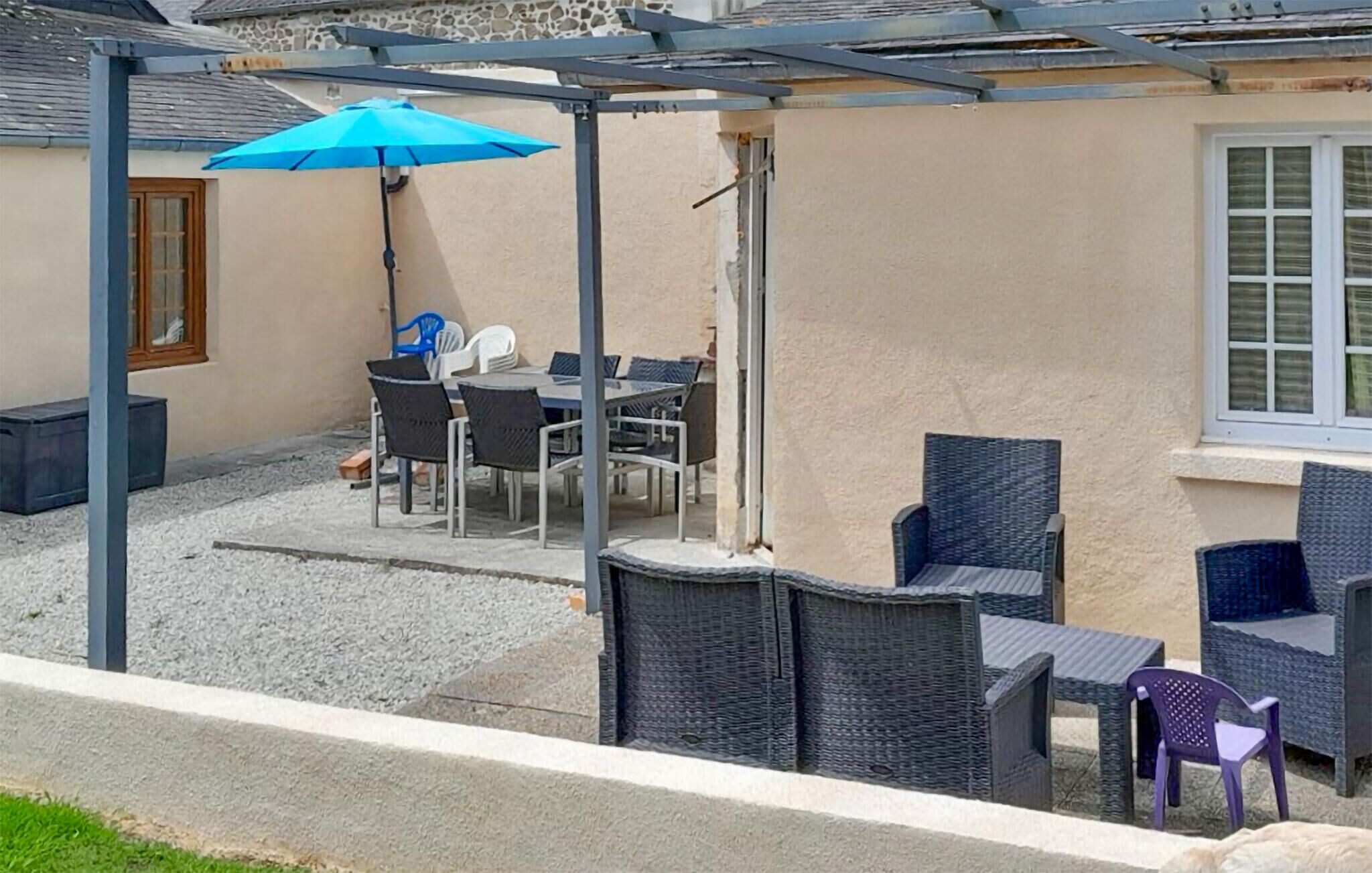 A covered outdoor seating area with a table and chairs, a blue umbrella, and a stone wall.