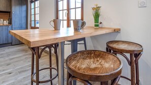 Eine Küche mit einem Holztisch, zwei Hocker, einer Kaffeemaschine und einer Vase mit Blumen.