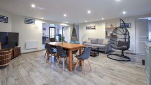 Ein modernes Wohnzimmer mit Esstisch aus Holz, grauem Sofa und einem Hängekorbstuhl.
