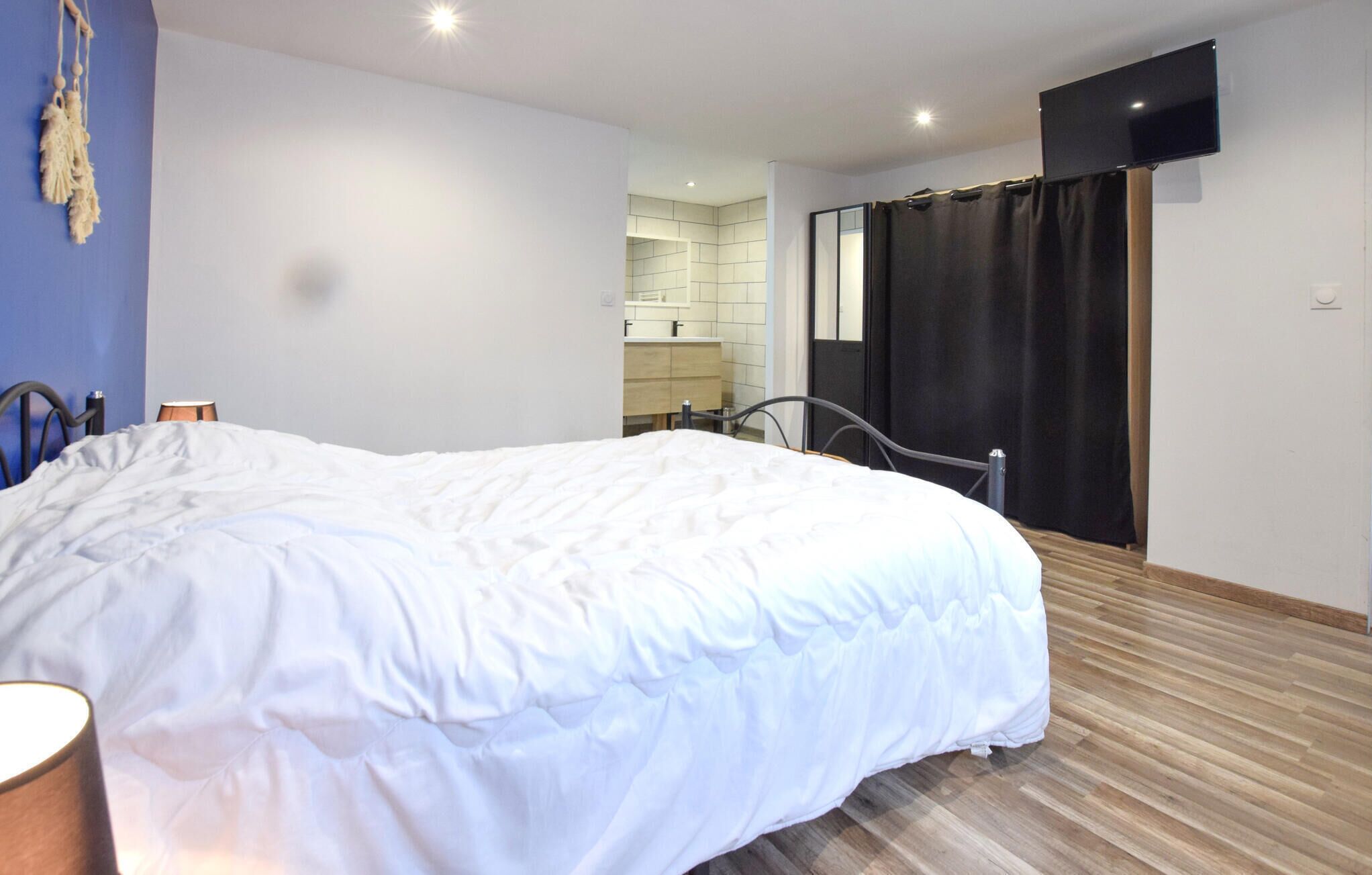 A bedroom with a large bed, a bedside lamp, a TV mounted on the wall, and a bathroom visible through an open door.