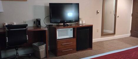 A hotel room with a desk, a television, a microwave, a trash bin, and a chair.
