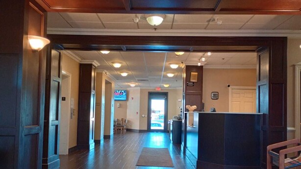 A hotel lobby with a wooden floor, a reception desk, and a TV screen in the background. - SAMIR Stay at NW Expressway (Oklahoma City)