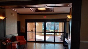 A lobby with a wooden floor, red chairs, and a large glass door leading outside. - SAMIR Stay at NW Expressway (Oklahoma City)