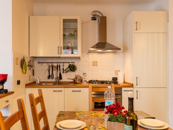 Una cocina con gabinetes blancos, una campana extractora de acero inoxidable, una estufa a gas, un lavabo y una mesa de comedor con sillas.
