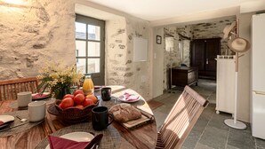 Een rustieke eethoek met een houten tafel gedekt voor het ontbijt, een stenen muur en uitzicht op de keuken.