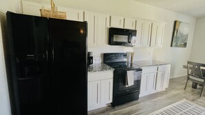 A kitchen with white cabinets, a black refrigerator, a microwave, and a stove.