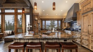 Une cuisine spacieuse dotée d’un grand îlot central, de meubles en bois et offrant une vue sur les montagnes.