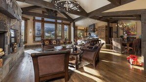 Un vaste salon doté de poutres en bois, d’une cheminée et offrant une vue sur les montagnes.