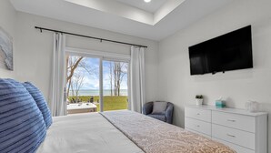 Un dormitorio con cama, televisión, sillón y vista al exterior.