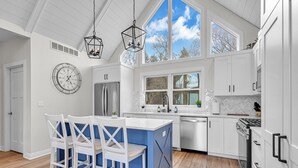 Una cocina moderna con armarios blancos, una isla azul y un amplio ventanal que proporciona luz natural.